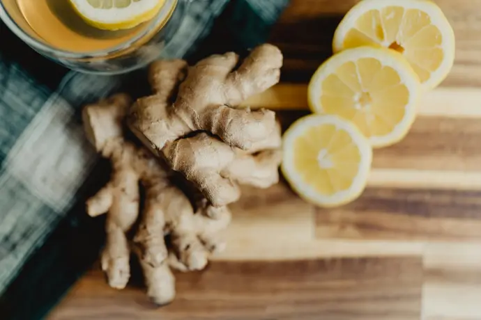 a glass of orange juice next to sliced lemons and ginger
