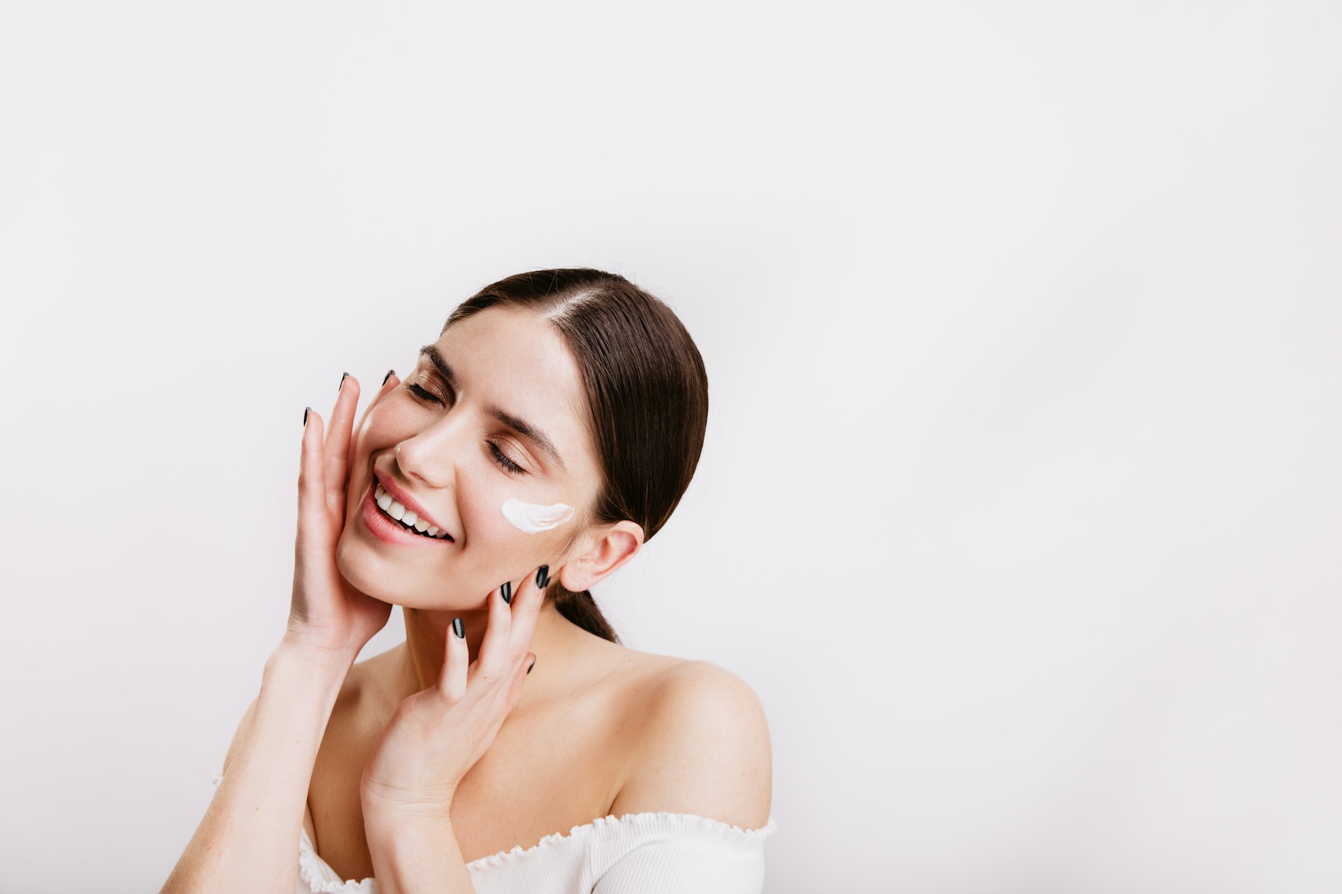 A woman in a white dress smiling and touching her face